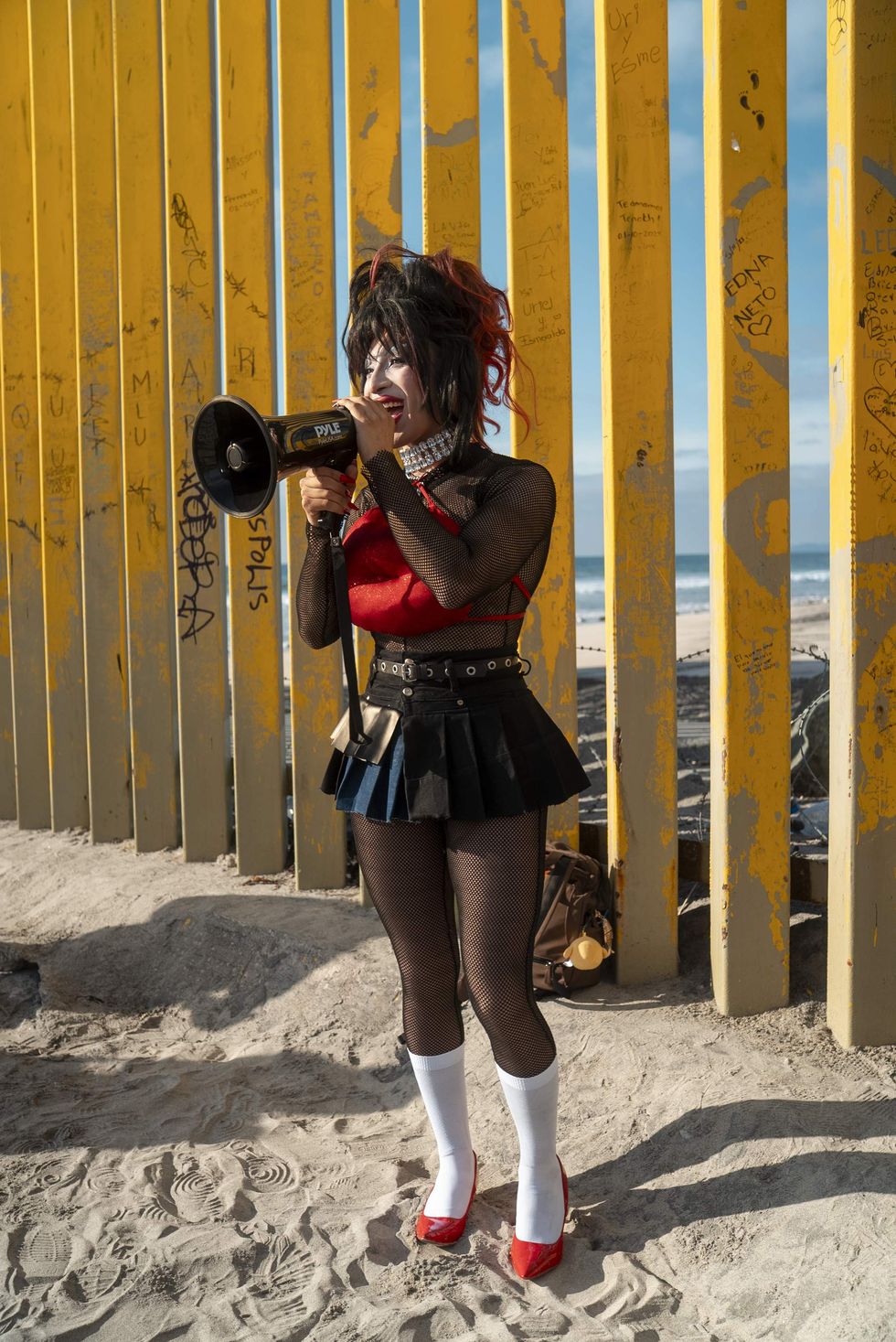 Drag queen giving a speech with a megaphone in front of the US-Mexico border