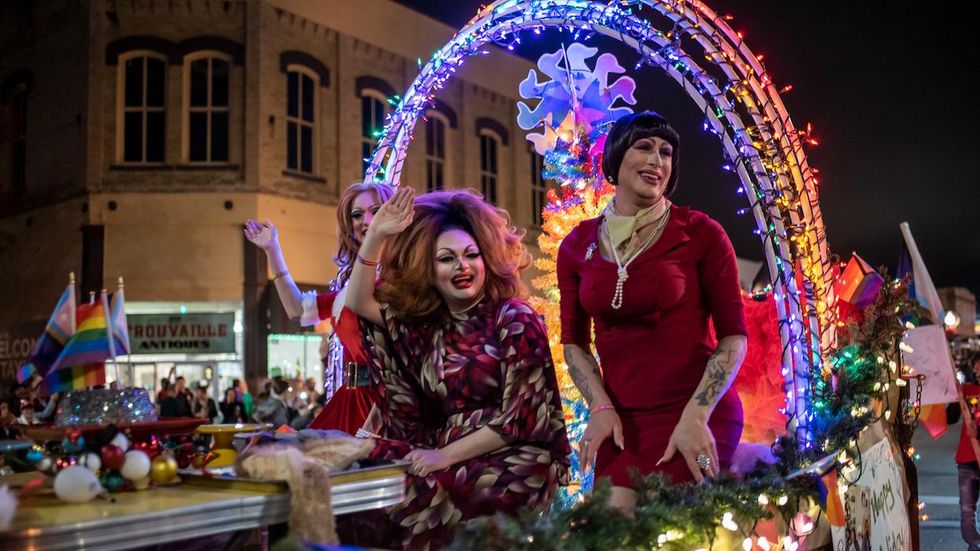 Drag queens in a float smiling and waving
