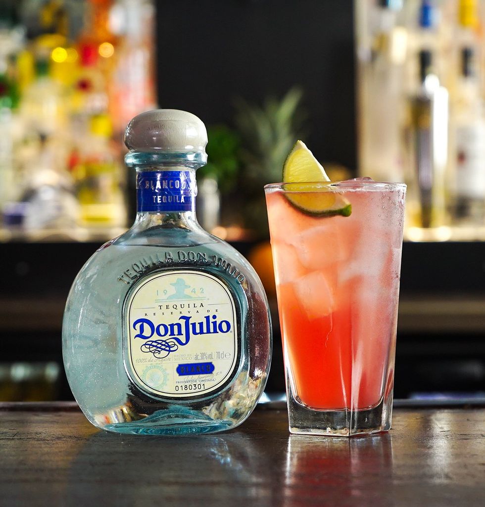 El Diablo cocktail with lime garnish made with Don Julio tequila in tall glass on bar surface with bottles in background