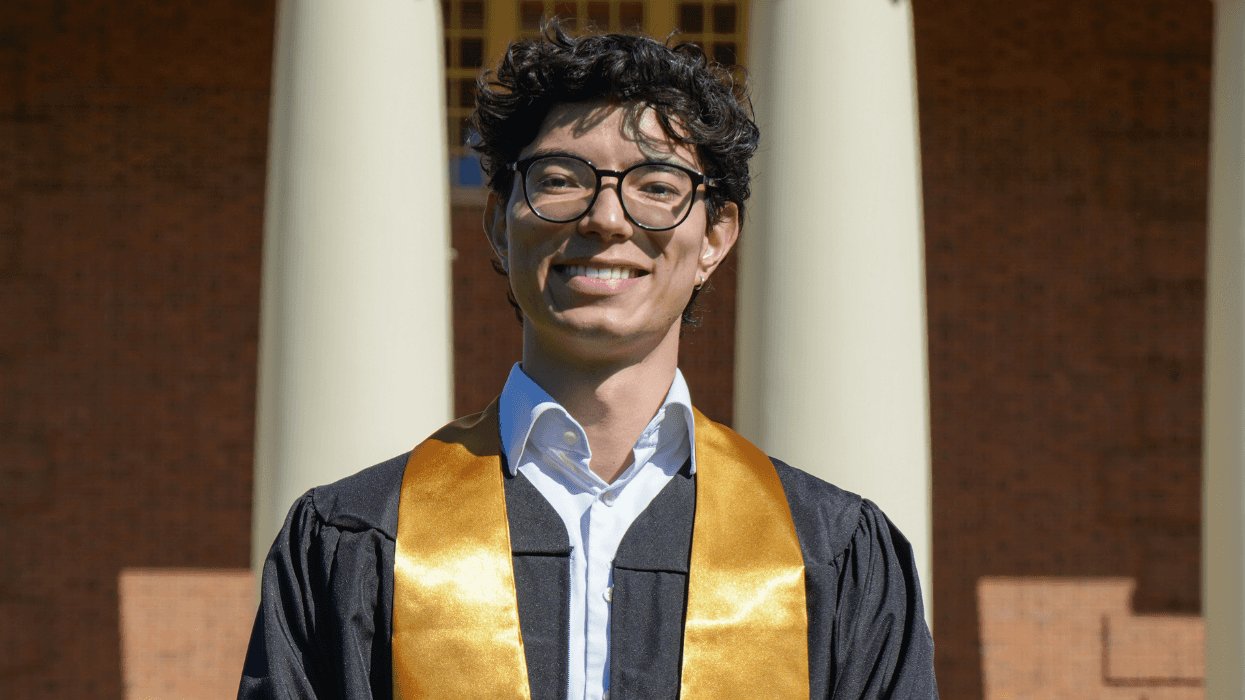 Eli Leadham poses in graduation regalia outside a campus building at Wake Forest University