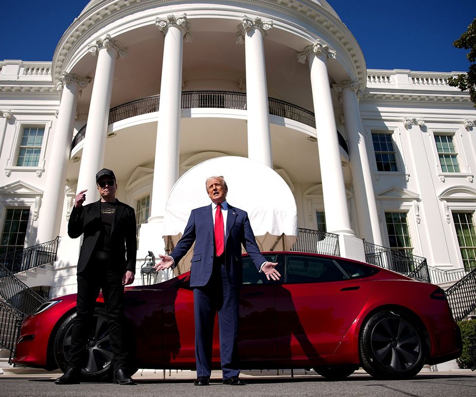 Elon Musk pointing to his MAGA Hat in front of a red Tesla at the White House while Donald Trump speaks with his hands out like a salesman