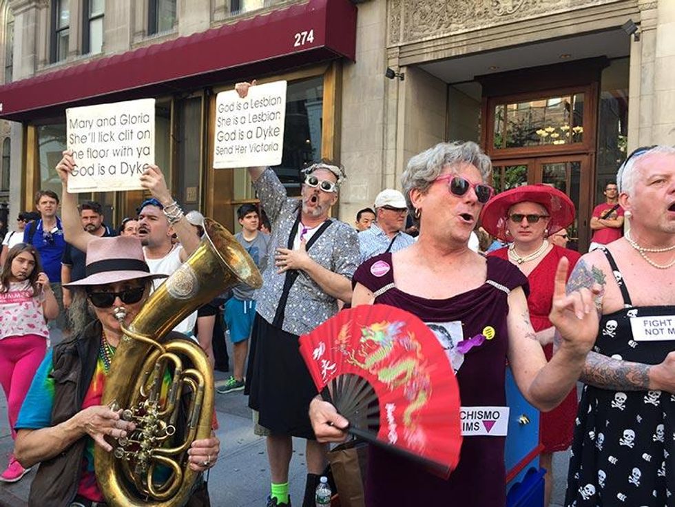 From the sidelines singers in drag croon "God Is a Lesbian."