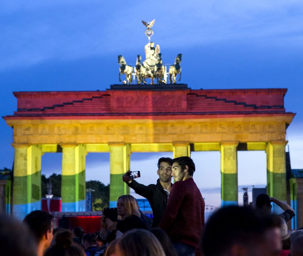 gay couple taking a selfie in front of the Brandenburg Gate lit up with LGBTQ rainbow colors Berlin Germany 2016
