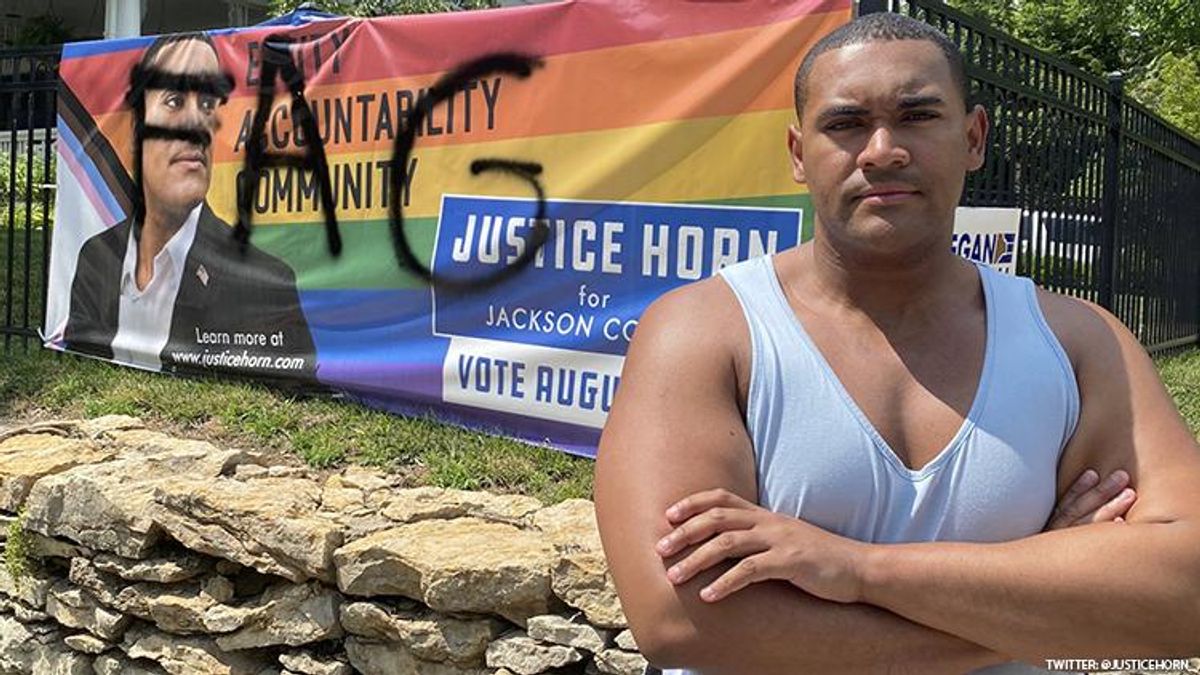 Gay former NCAA Wrestler Justice Horn stands in front of a campaign sign that was defaced with the word fag.