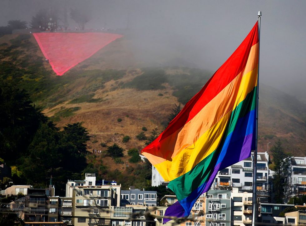 giant pink triangle on Twin Peaks San Francisco behind LGBTQ rainbow flag waiving in front of buildings