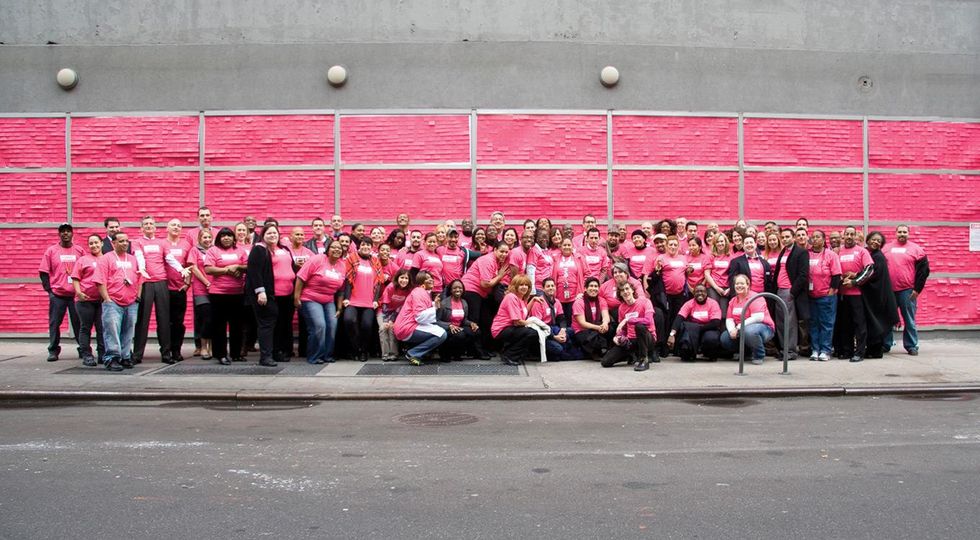 GMHC staff wear magenta in front of the GMHC building, whose windows are covered with magenta sticky notes, to celebrate its rebranding from red to magenta.