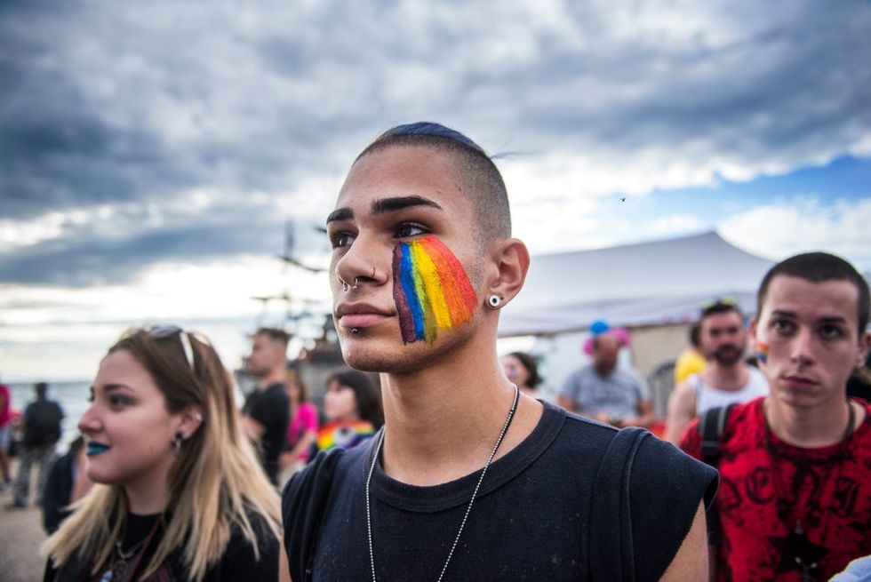 Greek man with his face painted in the colors of the Rainbow Flag