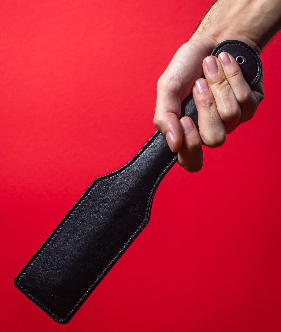 hand holding leather paddle against red background