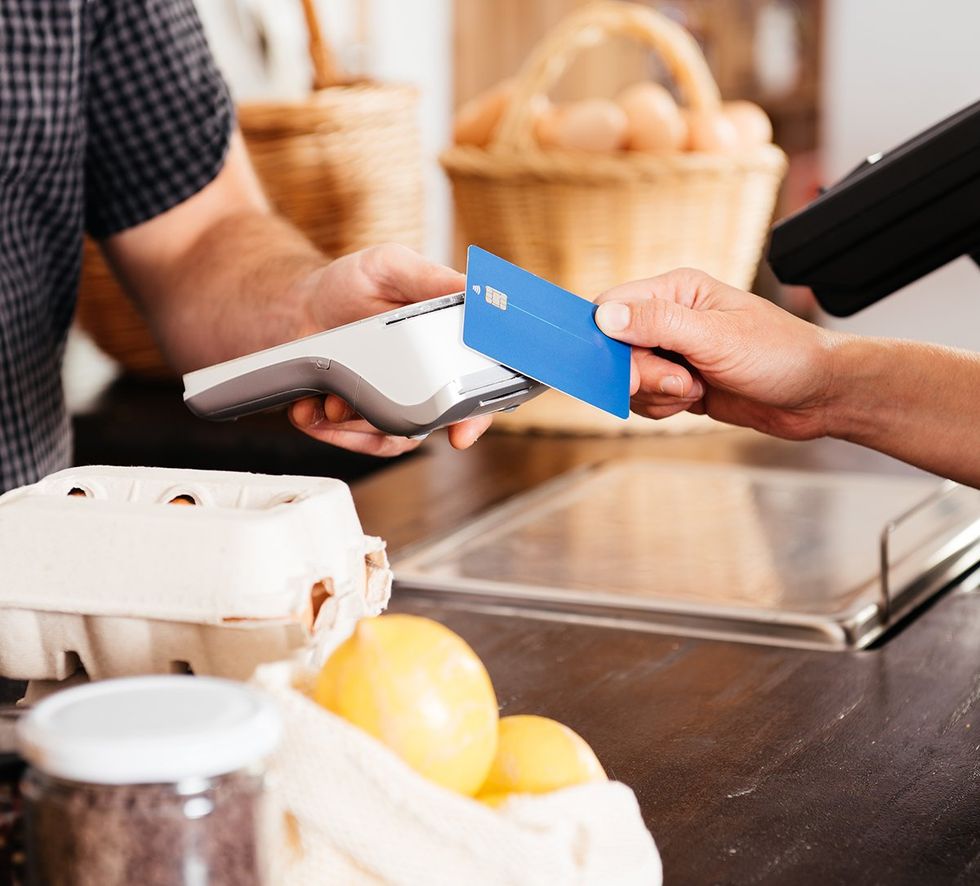 hand is seen giving a credit card to a cashier at a grocery store counter