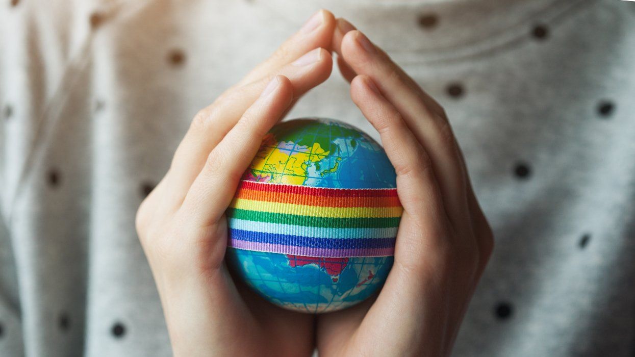 hands holding small globe wrapped in rainbow ribbon
