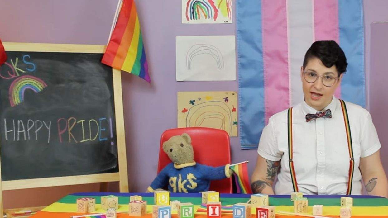 happy pride written on a chal board with a person in rainbow suspenders speaking before some pride flags