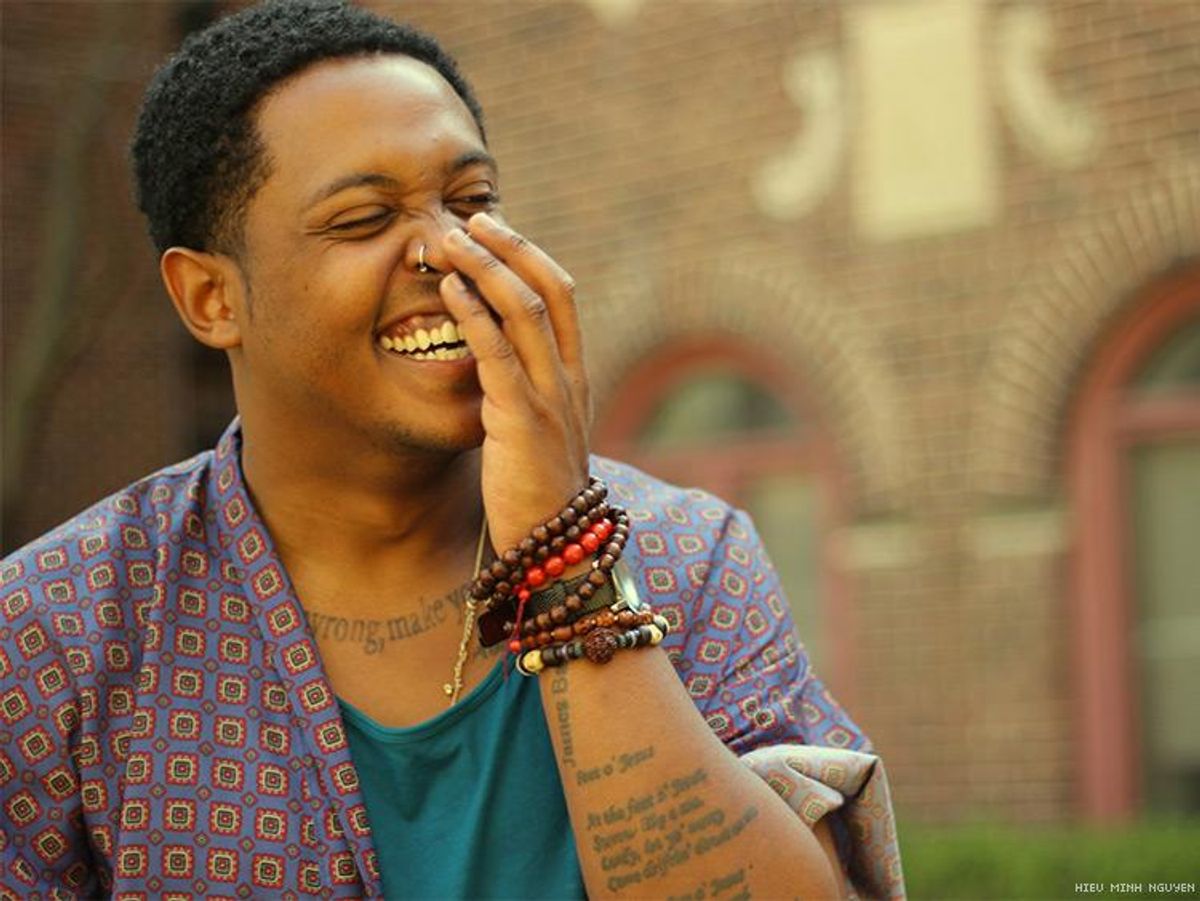 Headshot of Danez Smith, a black queer male poet, laughing and looking toward side of frame 