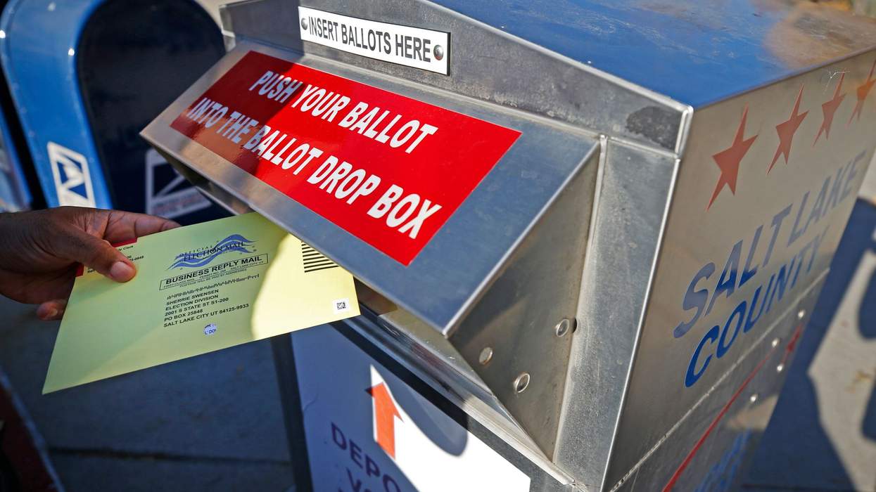 Image of a voter putting an envelope labeled "official election mail" into a slot in a large metal box that reads "push your ballot into the ballot drop box"