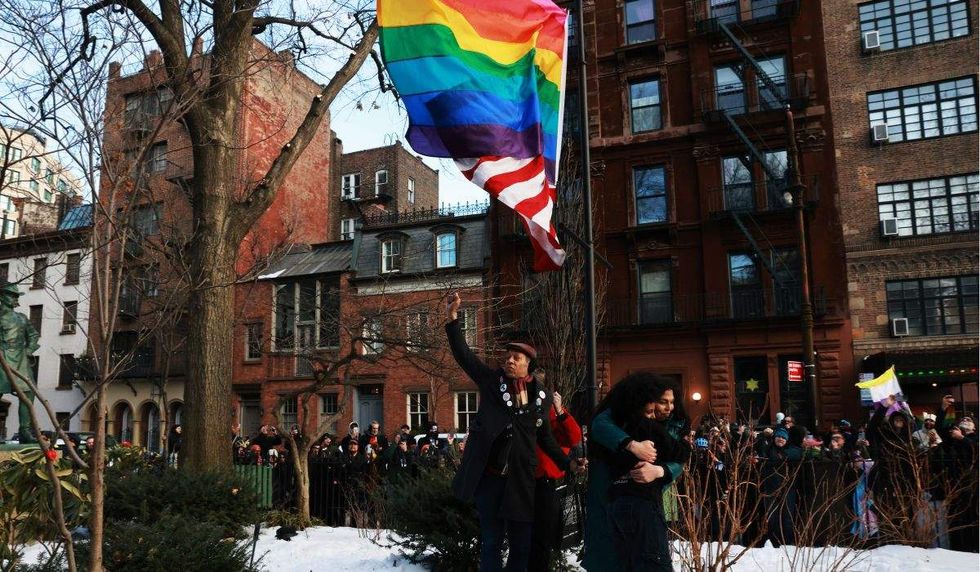 jay w. walker holds up his fist as two people hug below a pride flag and u.s. flag