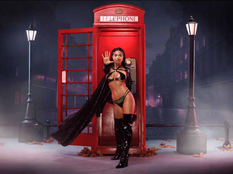 Jessica White poses in a black leather-inspired outfit and thigh-high boots in front of a red London telephone box dressed as The Matrix's Trinity on a moody city street