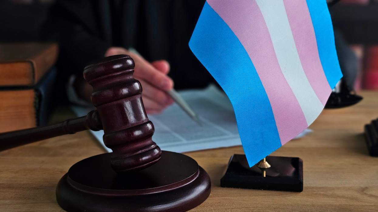 judge's gavel and transgender flag on a desk, with someone signing paper in the background