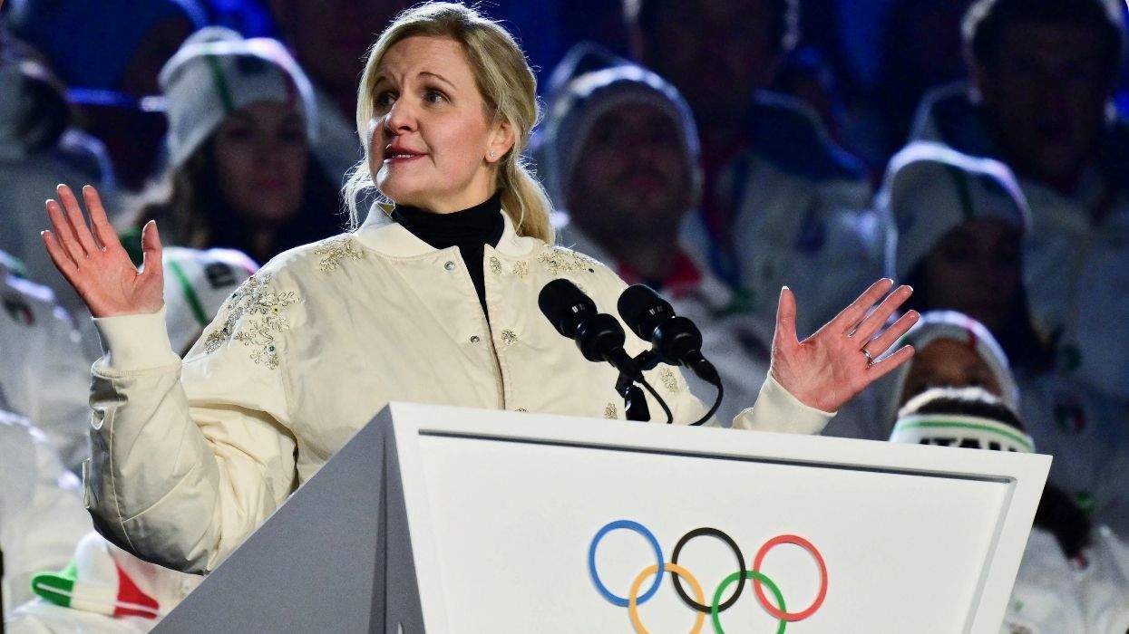 kristy coventry speaking at the olympics behind a lectern with the olympic rings
