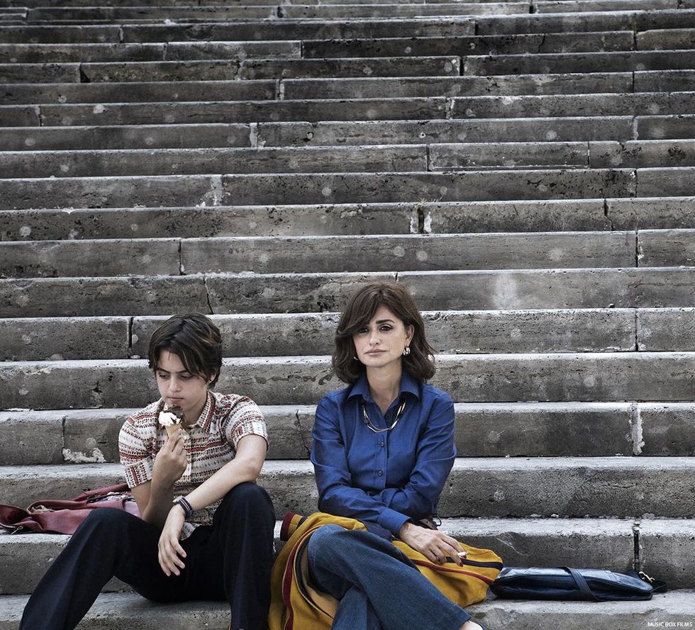 Luanna Giuliani as Adri and Penelope as his mother sitting on some steps. Adri is eating an ice cream while his mother smokes a cigarette.