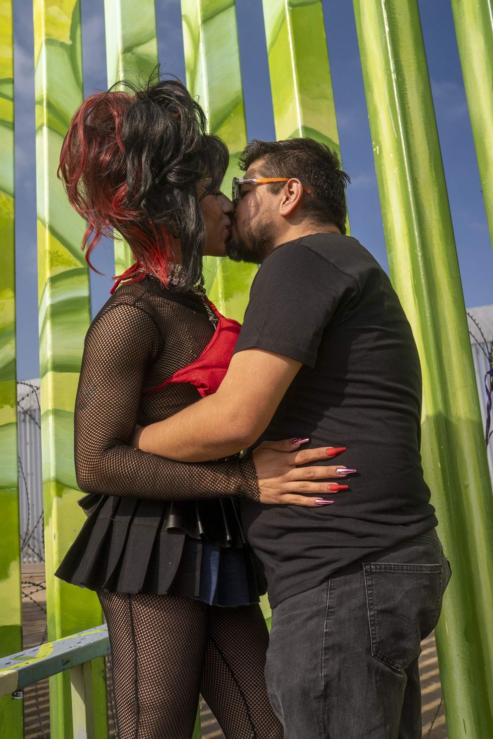 A man and a drag queen kiss in front of the US-Mexico border