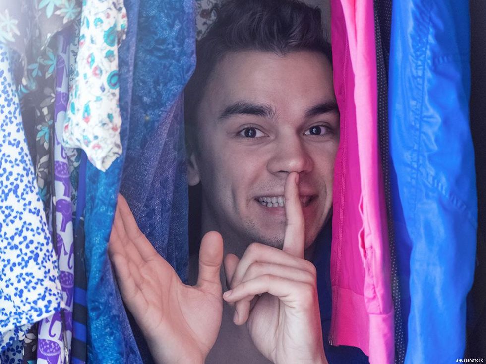 man in closet making shhh motion between clothes