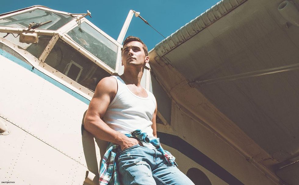 man in jeans and tank top leaning against a camper van