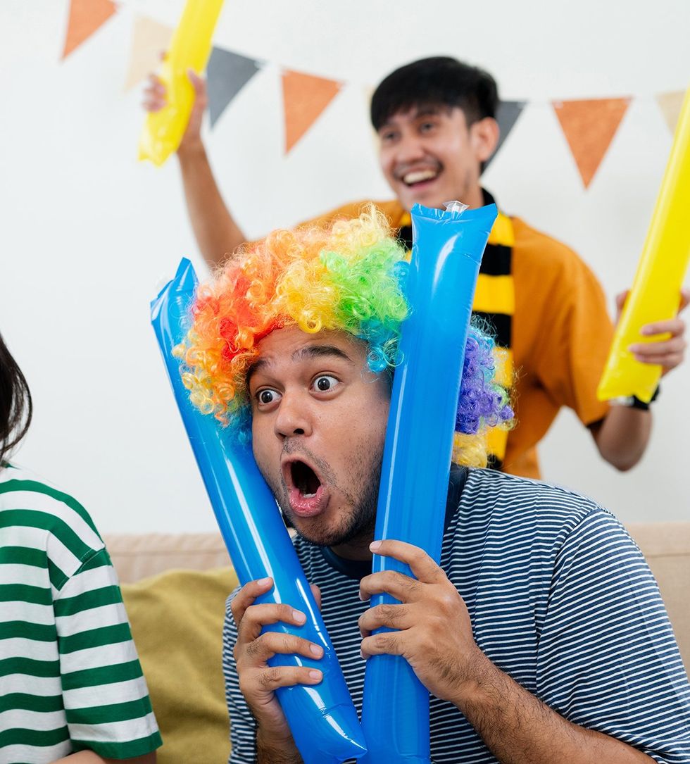 man in rainbow clown wig holding balloons playing party games
