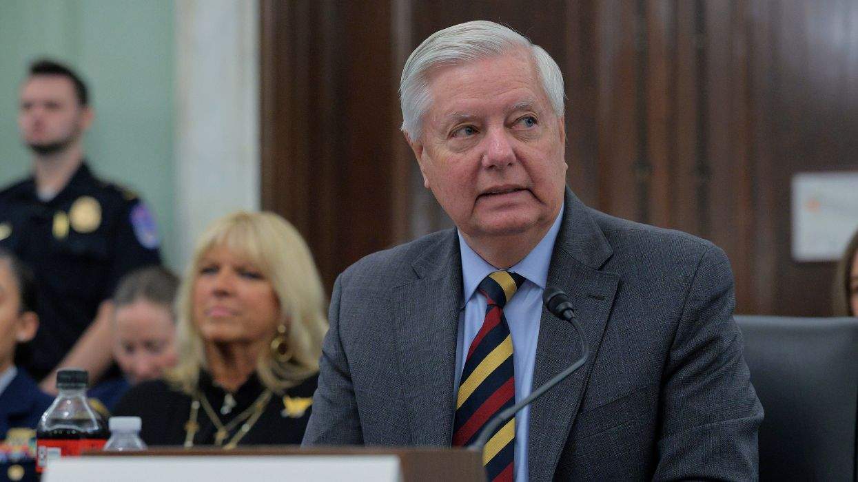 Man in suit speaking at a microphone in a formal setting.