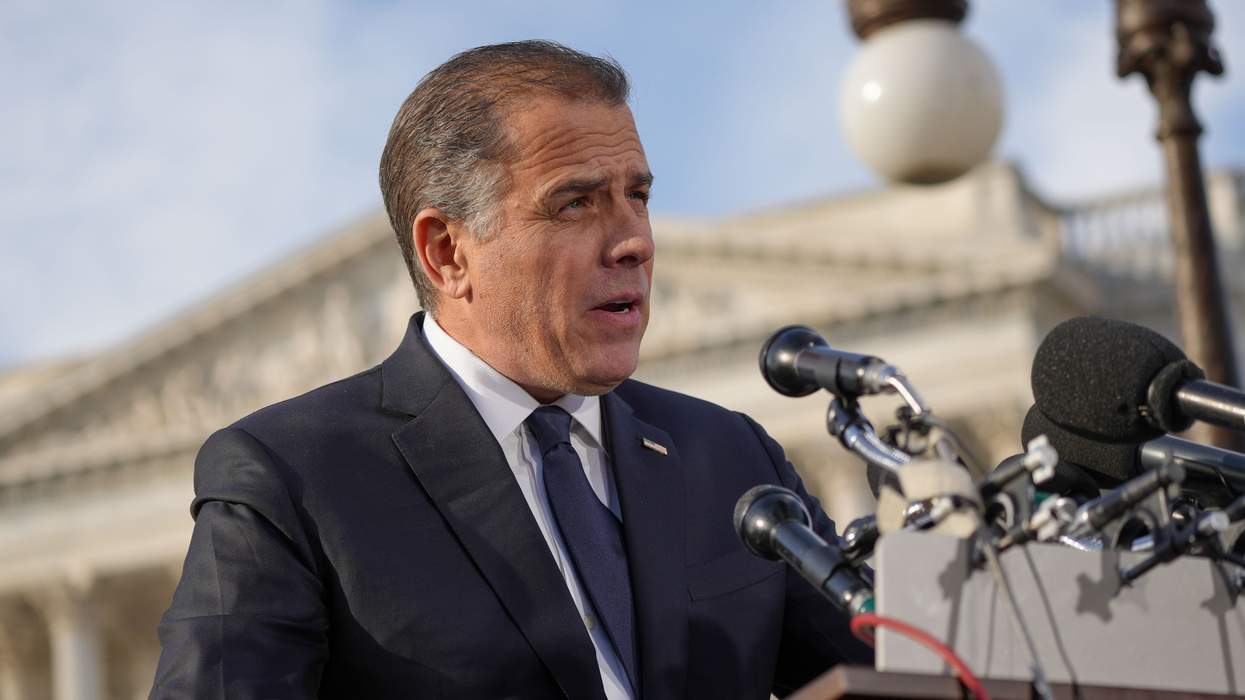 Man speaking at a podium with multiple microphones in front of a large building.