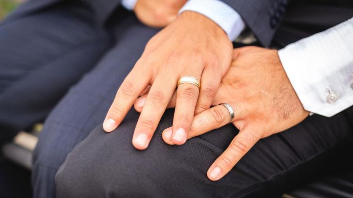 Married gay couple holding hands with their rings shown