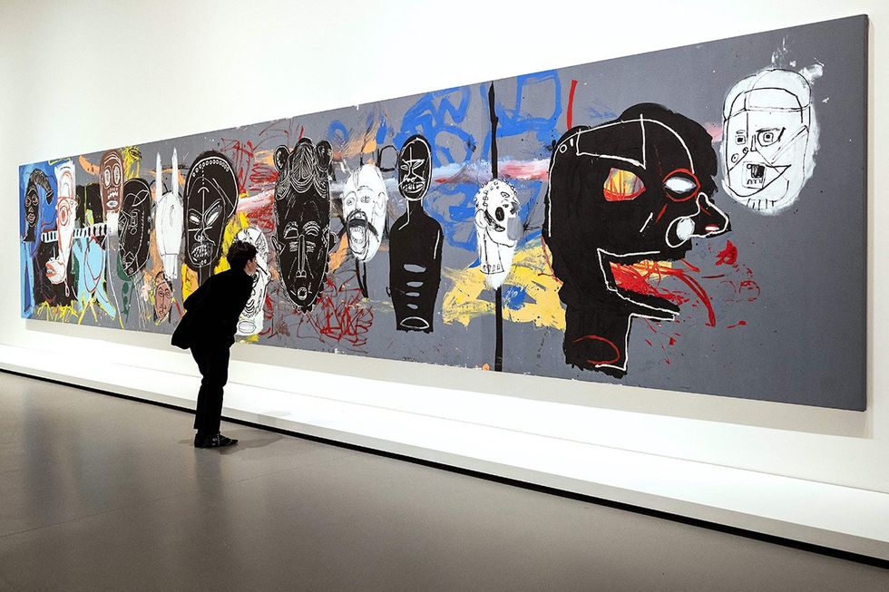 Museum visitor inspecting African Masks acrylic circa 1984-1985 collaborative painting by Jean Michel Basquiat and Andy Warhol
