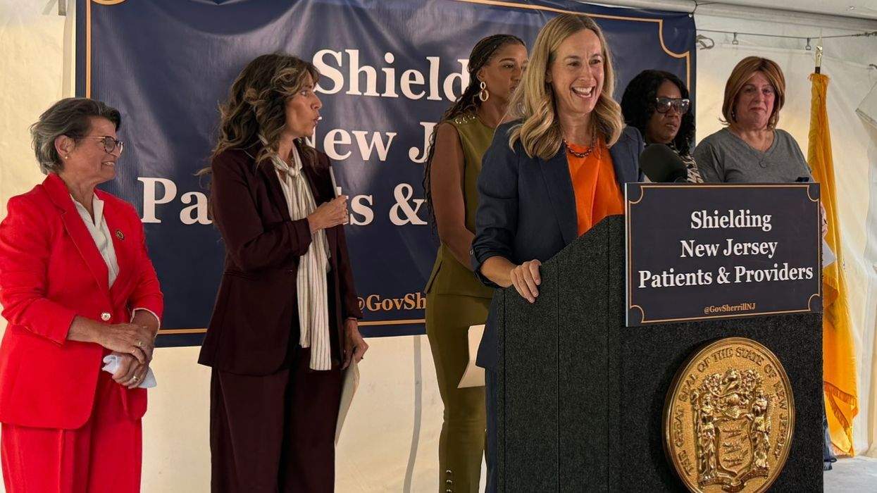 new jersey governor mikie sherill speaks behind a lectern with a sign that says shielding new jersey patients & providers