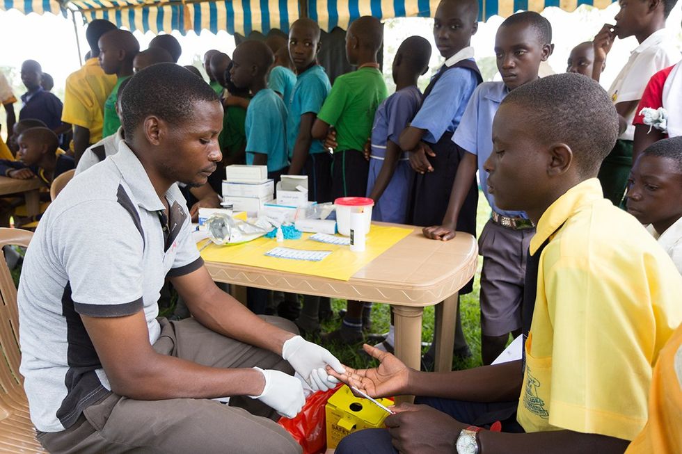 Nkokonjeru Uganda 2017 young man testing a boy for HIV by pricking his finger and drawing blood.