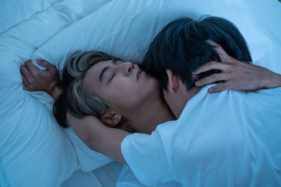 One man kissing another man's neck while lying in bed.