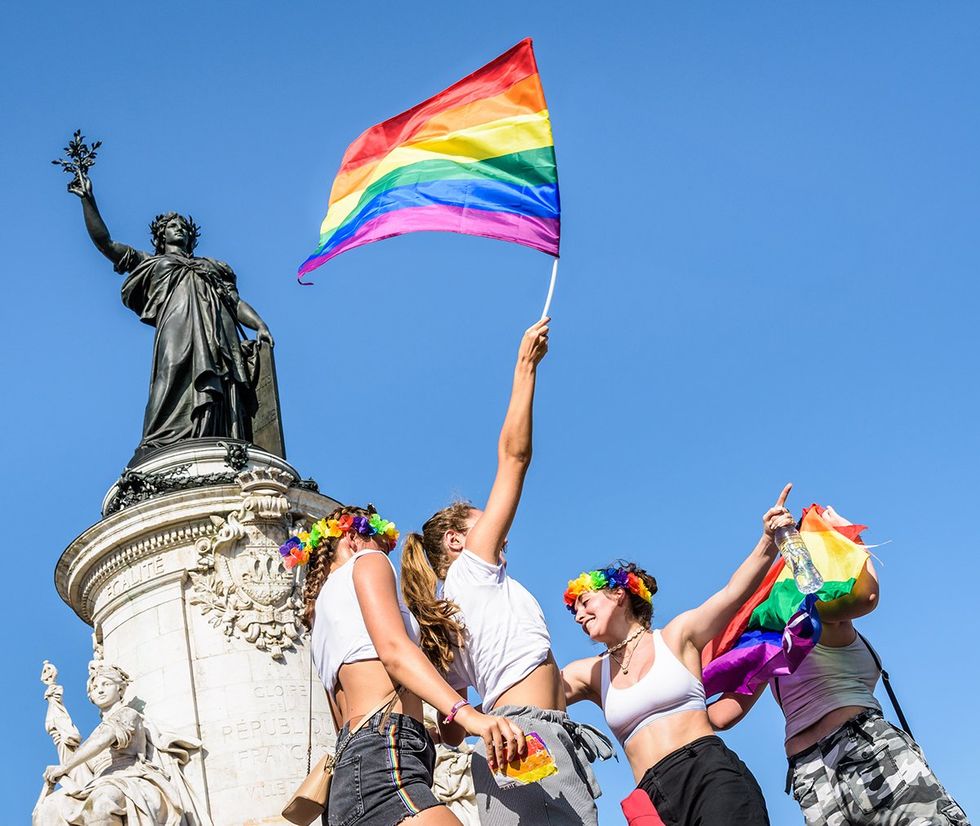 Paris France 2019 young women rainbow flag dance in the sun at the foot of statue Marianne on the place de la Republique LGBTQIA Pride parade end