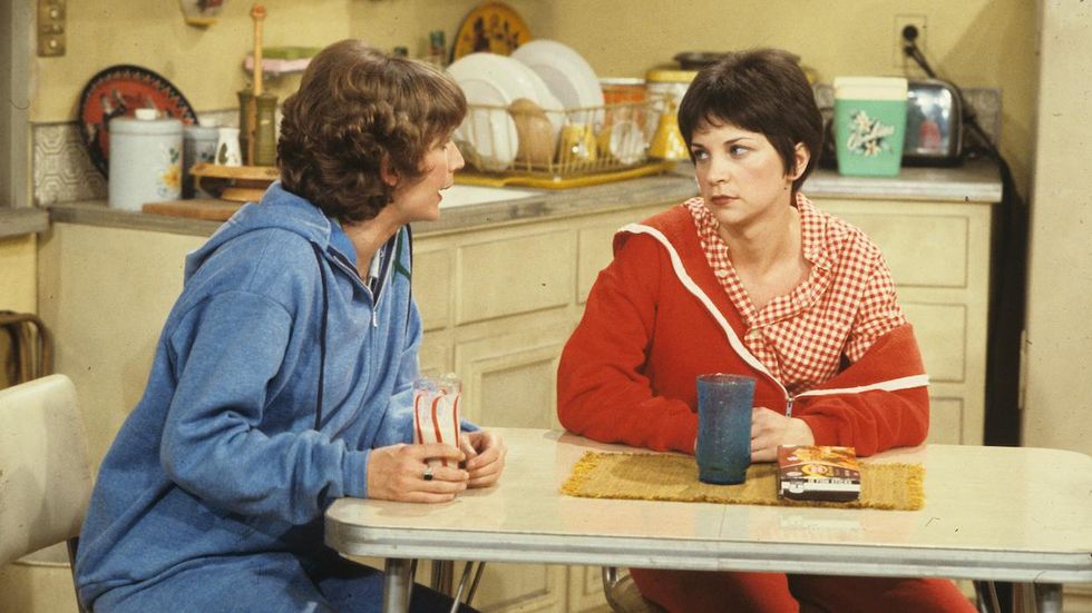 Penny Marshall and Cindy Williams in character as Laverne and Shirley sitting at a kitchen table