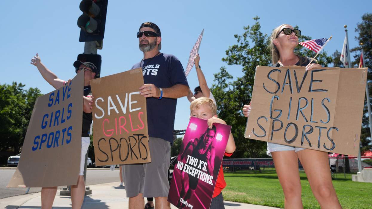 People hold signs in protest of transgender athletes participating in youth sports