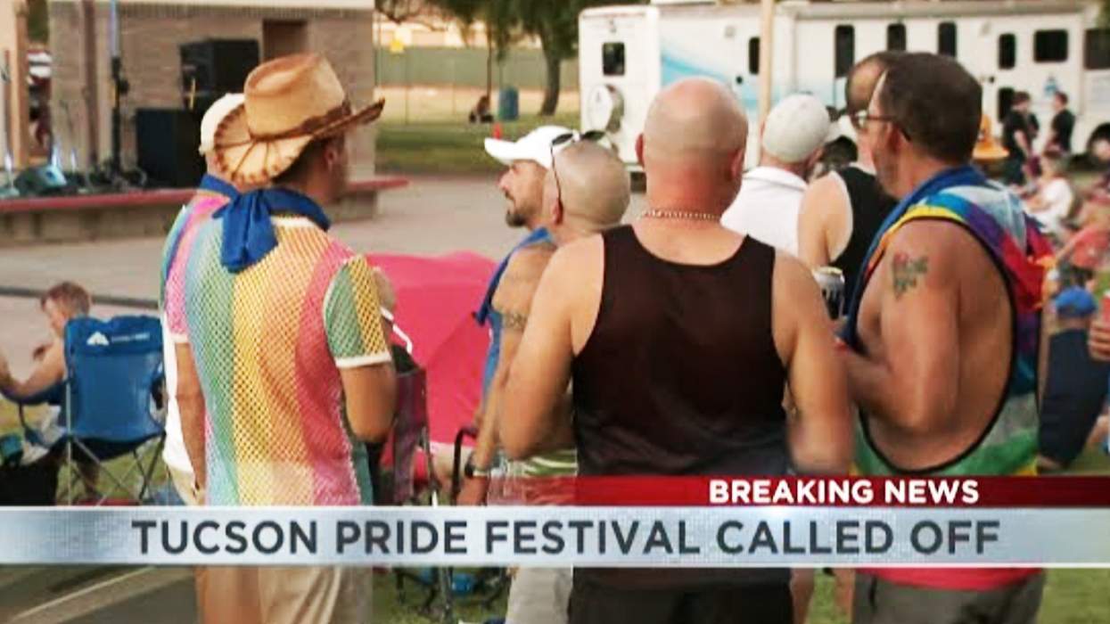 People in rainbow-colored clothing gather along a city street, where others sit in chairs and stand in the grass.