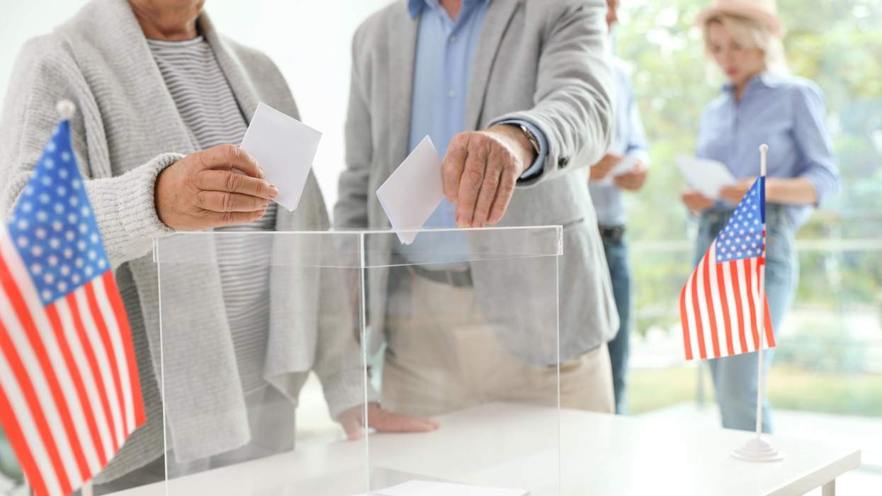 people putting votes into a ballot box with american flags nearby