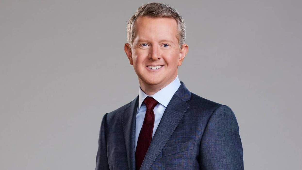 Person in a suit and tie smiling against a plain background.