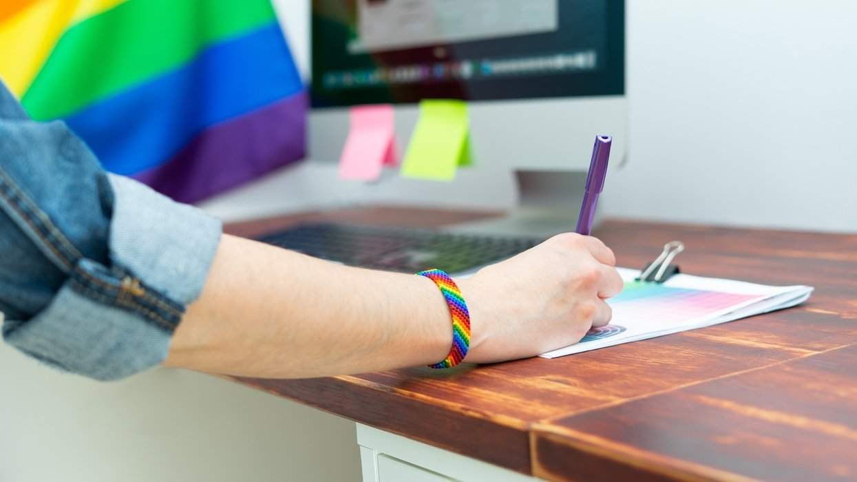 person with rainbow bracelet writing something down near a computer