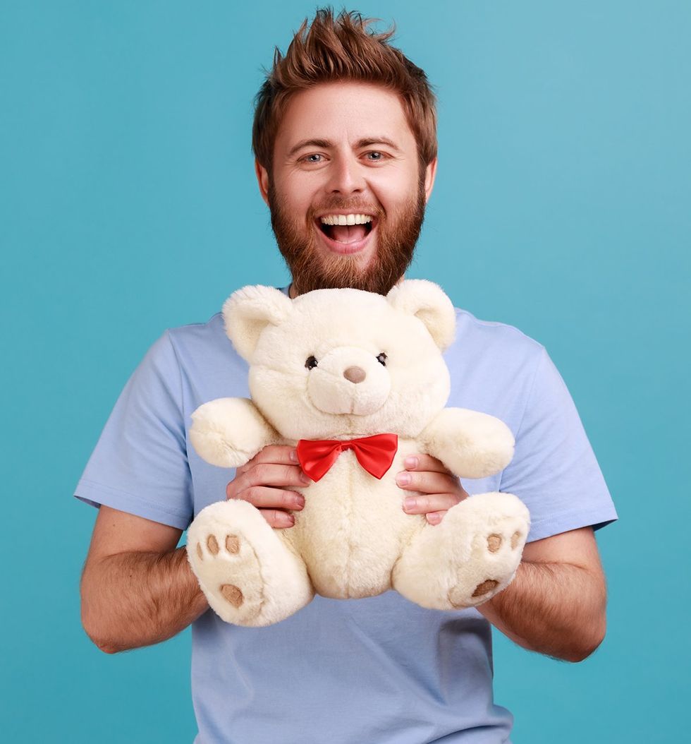Portrait of happy optimistic handsome bearded man standing looking at camera holding white soft teddy bear, expressing positive emotions
