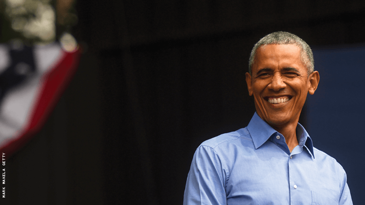 president obama, a black man with gray hair, is smiling near a flag