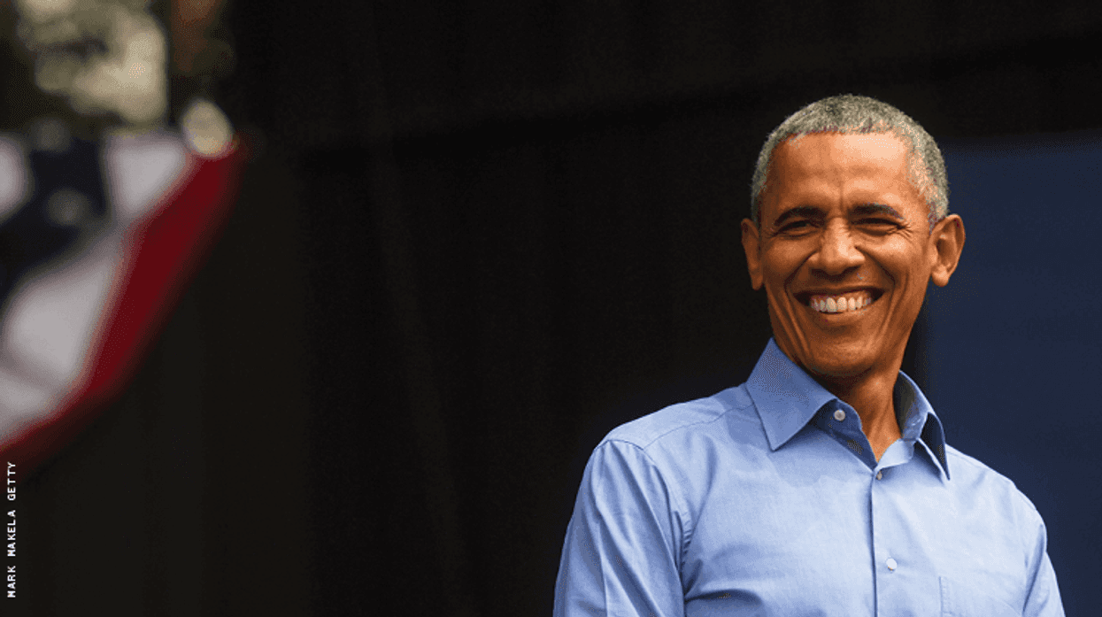 president obama, a black man with gray hair, is smiling near a flag