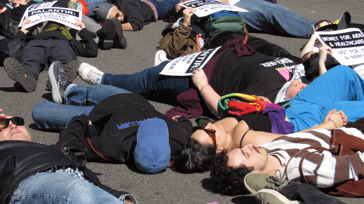 Protesters holding signs lie in a city street with their eyes closed.