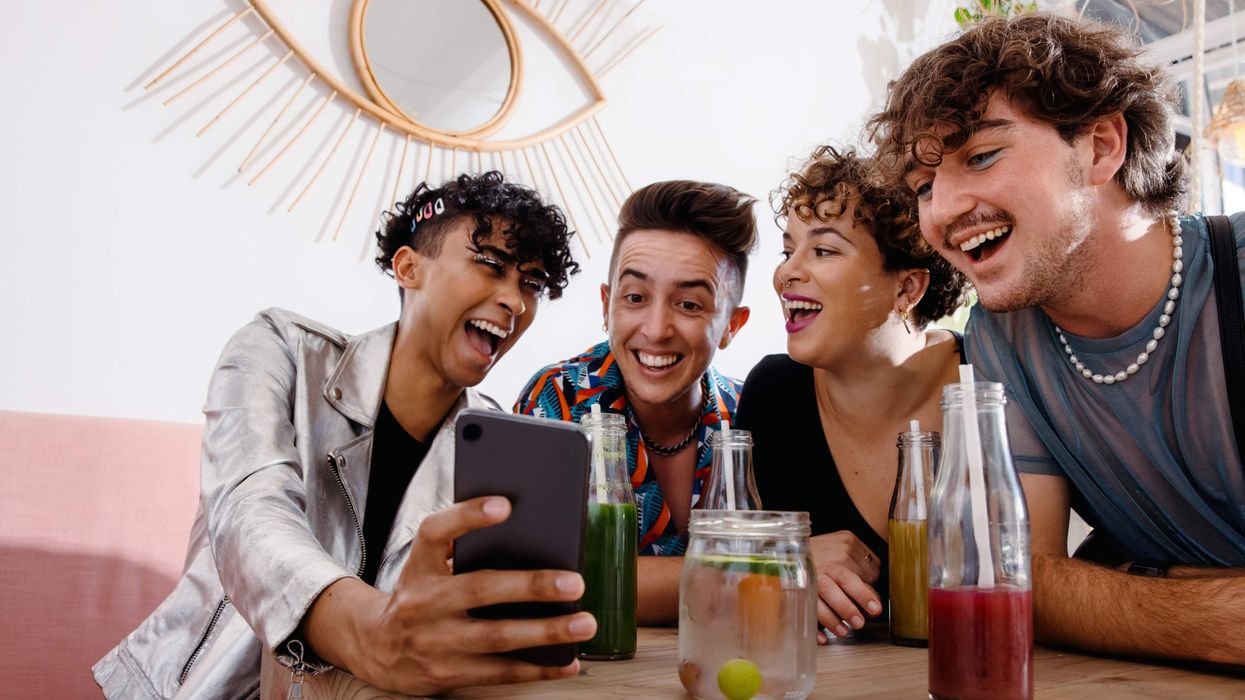 Queer friends siting around a table looking at a cell phone.
