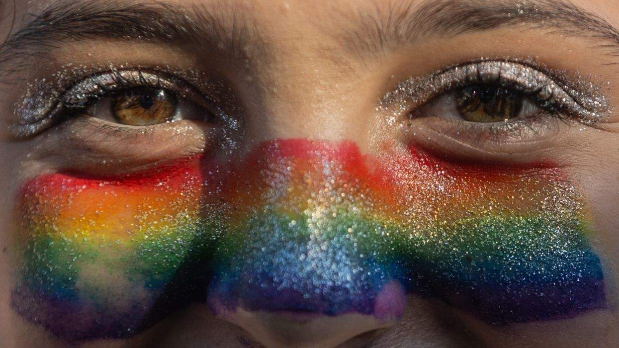 rainbow face paint and sparkels around a person's eyes very close up