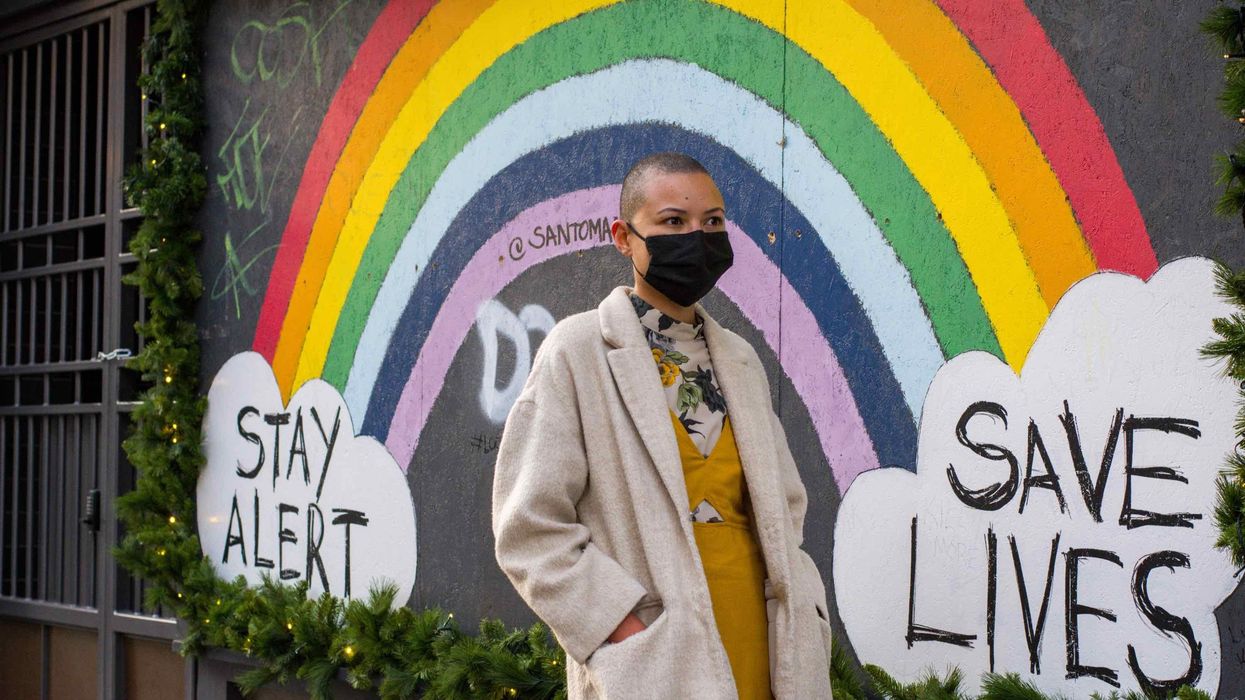 rainbow stay alert save lives poster behind a woman in a mask
