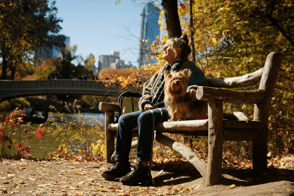Robin Byrd sits on a wooden bench in Central Park with her dog beside her.