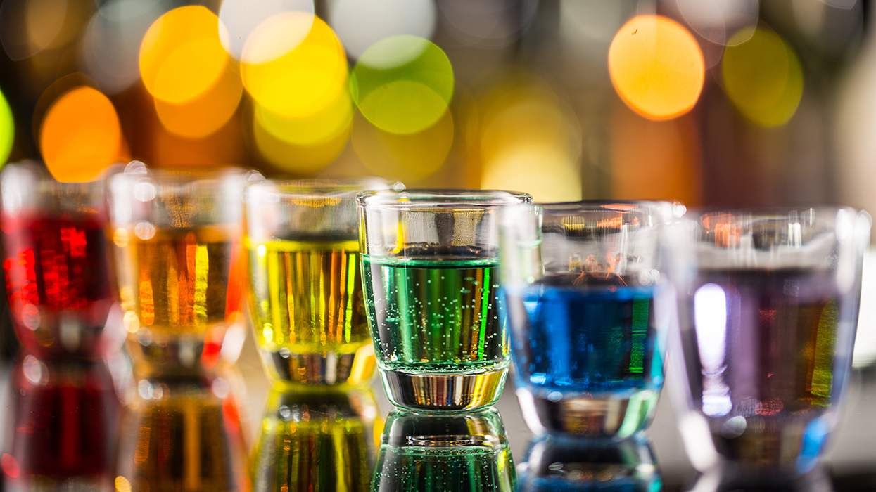 row of shot glasses filled with rainbow liquid on bar with selective focus on green and bokeh light background