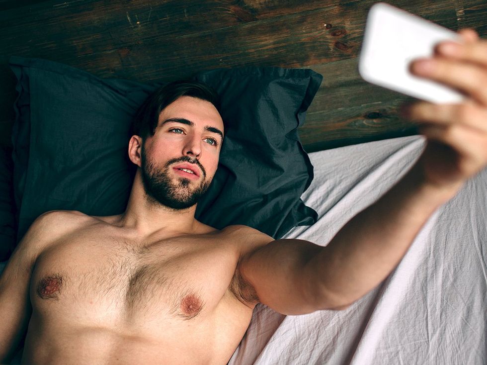 sexy gay man taking shirtless selfie in bed
